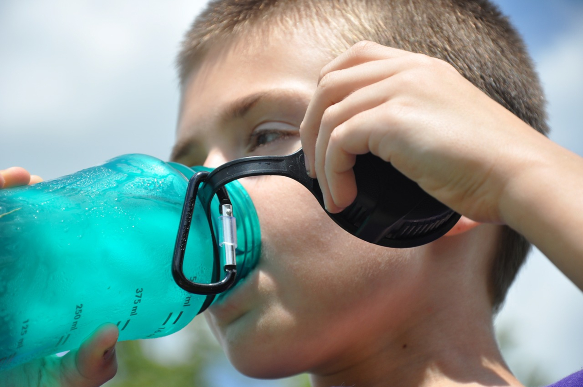 A white child drinks from a blue water bottle