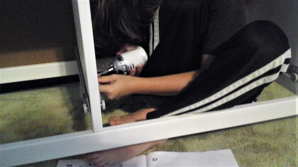Skinny 11yo scrunched into the frame of a tv stand being assembled, using an R2D2 screwdriver to secure an inner screw.