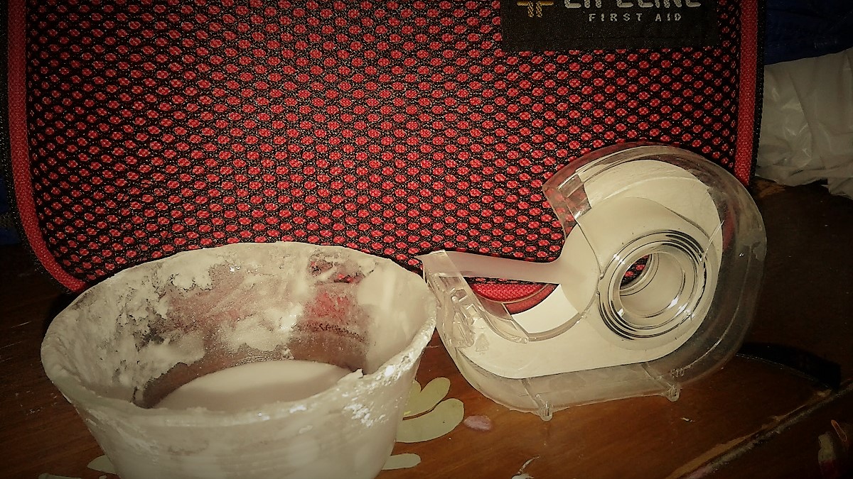 a dish of white goop (baking soda paste) and a roll of scotch tape in front of a first aid kit
