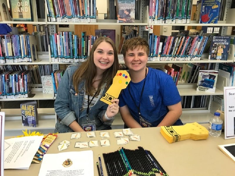 teens hold up a cardstock "Infinity Gauntlet" at a table full of scavenger hunt supplies