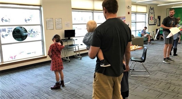 In foreground a girl aims a Nerf gun at a poster of the Death Star, more activities can be seen stretching out beyond